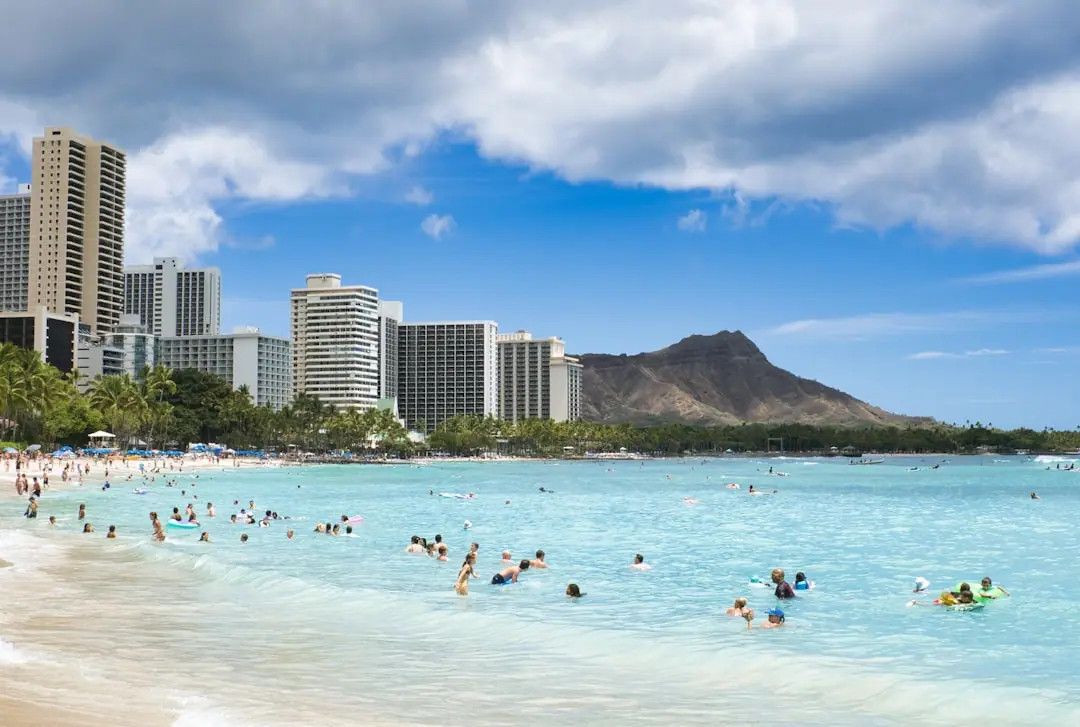 People swim in the ocean near a tropical beach with buildings.